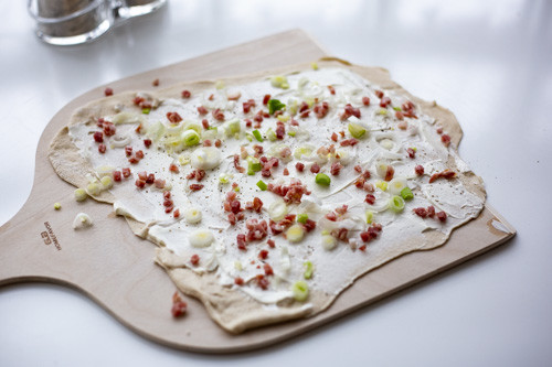 Pampered Chef Flammkuchen belegt auf Holzschuber vor dem Backen