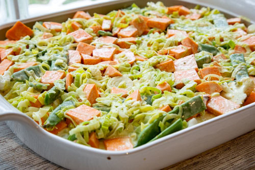 Pampered Chef flacher Bäker Süßkartoffel-Blumenkohl-Auflauf mit Zuckerschoten vor dem Backen mit Sauce übergossen